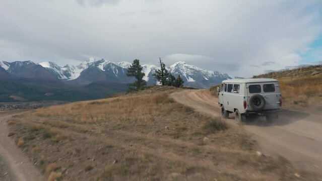 Gray offroad car microbus driving on rural road mountains valley, two spruces trees, autumn steppes. Picturesque mountains snowy caps in wild nature. Road car trip, adventure travel tourism vacations