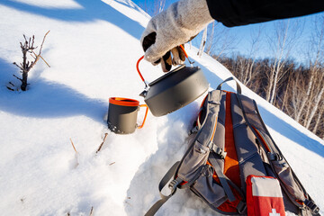 Camping equipment lies on the snow, a kettle with an aluminum mug, a hiking backpack, a first aid...