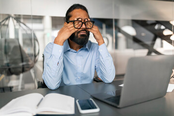 Tired young indian man employee suffering from sore eyes