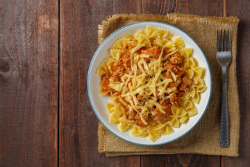 Bolognese pasta in a plate on a linen napkin next to a fork on a wooden table with a copy space