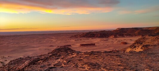 Panoramic sunset view from Timimoun, Algeria, overlooking the red sand desert and canyons from a hilltop.