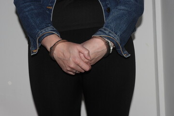 A close up of a woman's hands in handcuffs after she has been arrested. The woman is waiting to be...