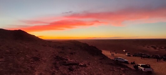 Naklejka premium panoramic view from the top of the hill over the red sand desert and canyons, crossed by off-road cars at sunset. Timimoun, Algeria