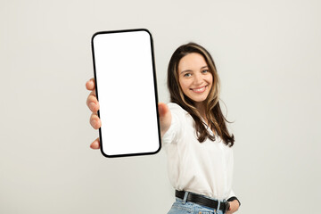 Smiling young brunette woman in a white blouse presenting a smartphone with a blank screen