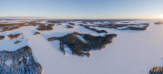 Aerial view over snow covered taiga landscape with boreal forest and frozen lakes in south Lapland, Finland at sunset
