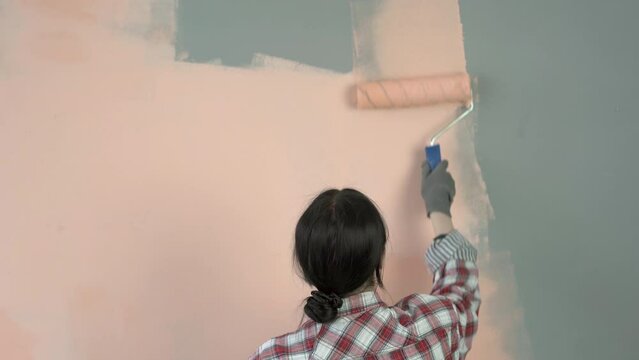 Home makeover and renovation. Back view of young woman painting her new apartment interiors using paint roller