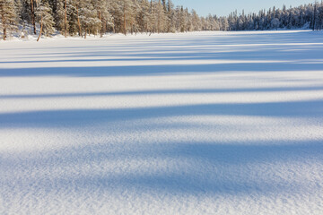 Winter in Finland; a low sun casts long shadows on a snow covered frozen lake in Oulanka National Park. 