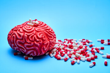 Representation of a red brain with a pile of red and white pills on a blue surface. Concept of addictions.