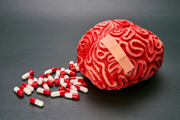 Depiction of a red human brain with a pile of capsules, pills and a band-aid on a dark background.