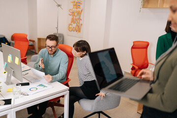 Focused male mentor and female intern sitting at desk with laptop doing paperwork together...