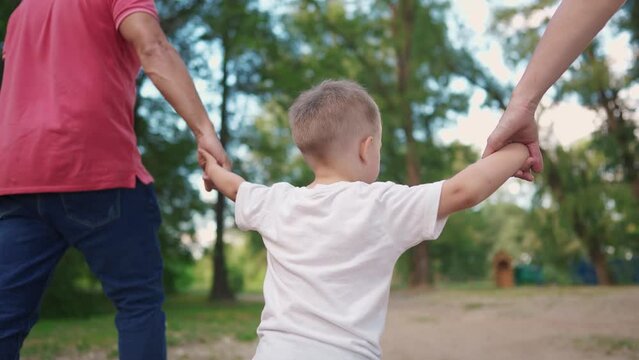 happy family in the park. a child walks with his parents holding hands, view from back in park in nature, walking. happy family kid dream concept. child son walking with parents in sun park
