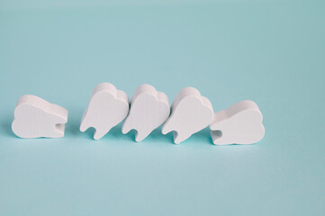 Crooked and uneven teeth concept. Row of toy wooden teeth on a turquoise background. Problematic...