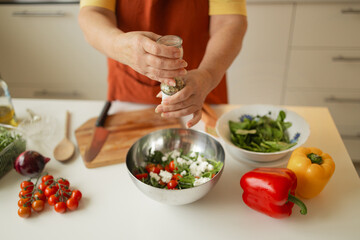 Close up of senior woman is preparing vegetable salad in the kitchen.Female adding arugula to salad. Healthy Food. Vegan Salad. Diet. Dieting Concept. Healthy Lifestyle. Cooking At Home. Prepare Food