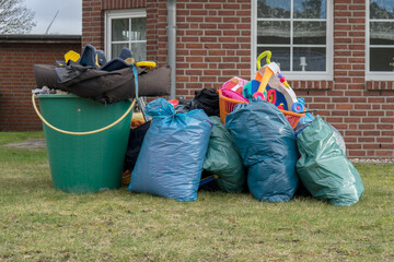 Pile of bulky waste in front of a house with garbage bags, rain barrels and toys