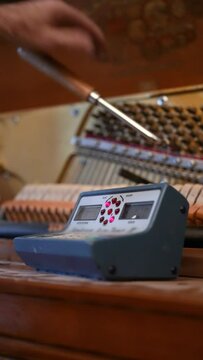 A vertical closeup view of a piano tuner working on an upright piano in a home.  	