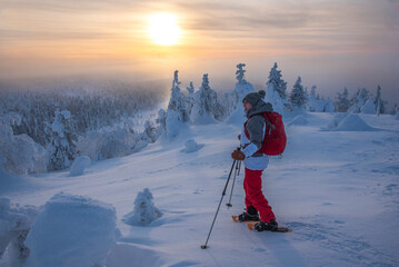 Woman snowshoeing at sunset on a mountain in Lapland Finland