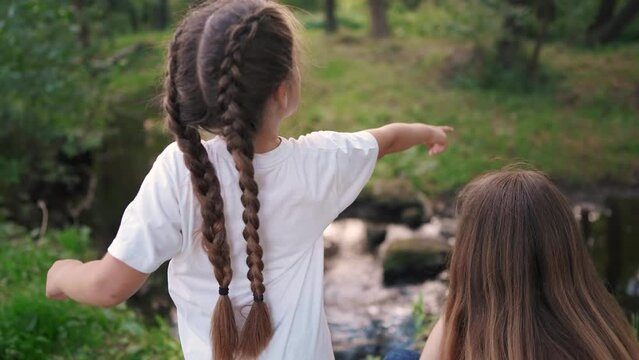 girl child plays with a group of friends in the forest in the park by the river. happy family dream content. girls child having fun in glare of the sun. girl with braids lifestyle