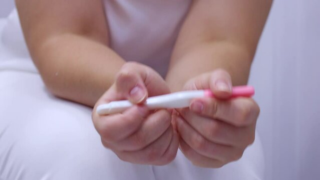 Woman hands holding pregnancy test waiting for positive result in bathroom. Girl checking plastic test kits at home. Fertility and healthcare concept