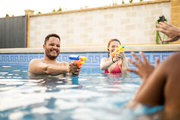 A young couple of different ethnicities has fun in the swimming pool of a country house.African man and Caucasian woman shoot with a water gun.Concept of playing in swimming pools in summer.