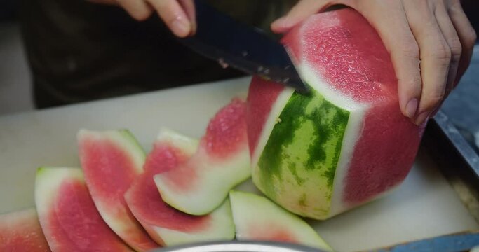 Close-up of hands cutting a fresh watermelon on a kitchen countertop, slices ready to serve.