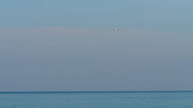 Airplane approaching to land. Airliner flies over the blue sea, descent. Passenger carrier in the sky, long shot