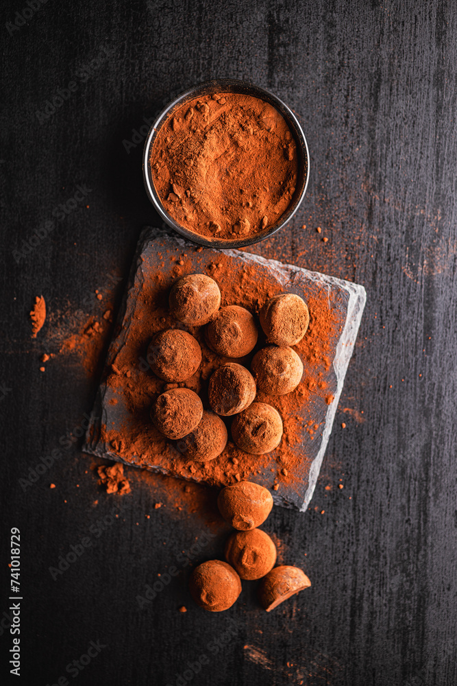 Poster Chocolate truffles covered with cocoa powder on black table. Top view.