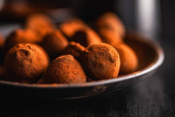 Chocolate truffles covered with cocoa powder on plate on black table.