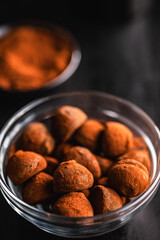 Chocolate truffles covered with cocoa powder in bowl on black table.