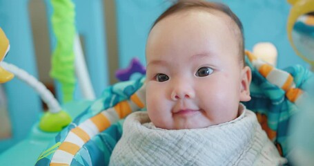 Portrait cute Bright-eyed Asian infant baby with a curious gaze smiling seated in a colorful baby bouncer indoor home, baby development playtime
