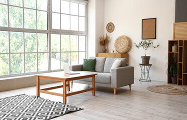 Interior of light living room with sofa and laptop on table