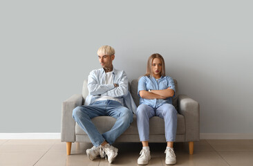 Offended young couple sitting on sofa near light wall