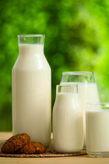 Bottles and glass of fresh milk with sweet cookies on yellow wooden table outdoors