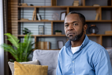 Thoughtful african american man sitting in a living room with a contemplative expression - obrazy, fototapety, plakaty