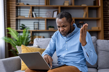 Frustrated african american man with laptop having technical difficulties at home