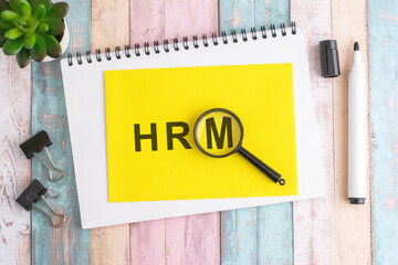 text HRM under a magnifying glass on a yellow background, top view, the text is written in black marker