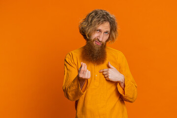 Give me money, please. Caucasian man rubbing fingers show cash gesture, demands to pay back the debt take loan do shopping begging investment reward. Redhead young guy isolated on orange background - obrazy, fototapety, plakaty