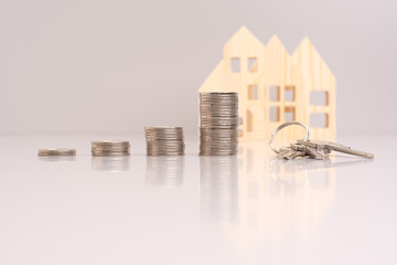 Stack of coins and a key on a gray background with model house with reflection