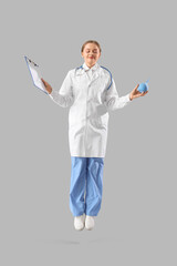 Female doctor with clipboard and enema jumping on light background