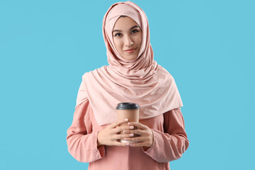 Beautiful Muslim woman with cup of coffee on blue background