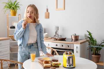 Young beautiful woman eating tasty toast with peanut butter in kitchen