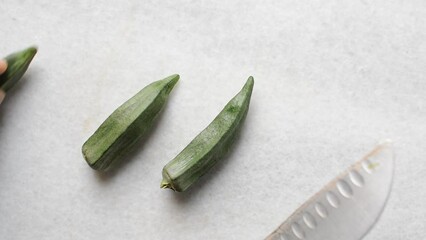 Top view of cutting okra on a white background, lady fingers being chopped on a marble countertop, okro being prepared for cooking
