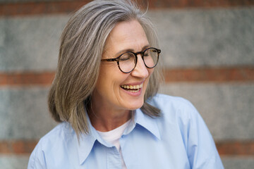 A happy older woman with glasses wearing a blue shirt.