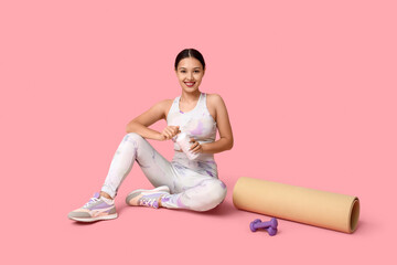 Young woman in sportswear, with bottle of water, dumbbells and yoga mat on pink background. Weight loss concept