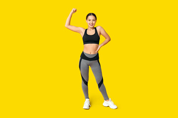 Fototapeta na wymiar Portrait of young woman in sportswear showing muscles on yellow background
