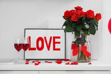 Frame with word LOVE, glasses of wine and red roses on white kitchen counter. Valentine's Day celebration