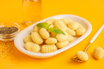 Plate with tasty gnocchi, basil, spices and fork on orange background, closeup