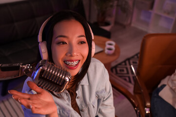Young Asian woman with microphone recording podcast in studio at night, closeup