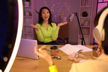Female Asian podcaster talking with guest in studio at night