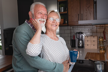 Beautiful senior married couple drinking coffee in the morning at home kitchen and sharing moment