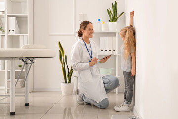 Pediatrician measuring height of cute little girl near white wall in clinic